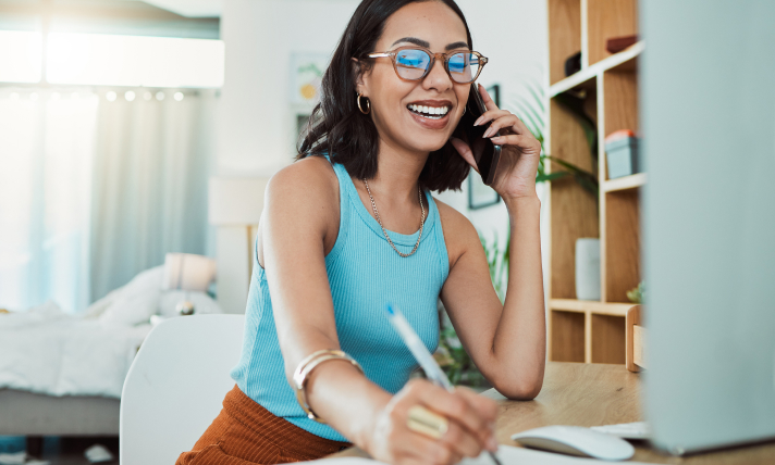 A woman talking on the phone while writing in a notepad.